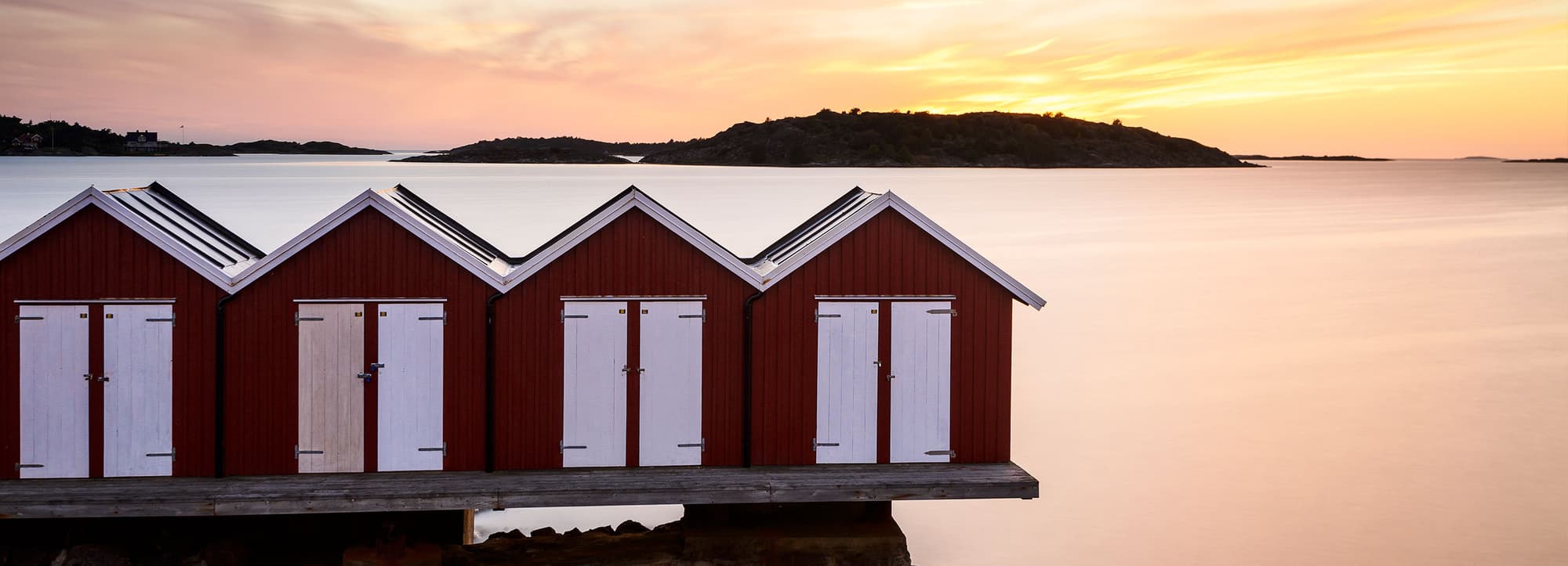 Svensk öl: Solnedgång i havet bakom små fiskebodar på en pir.