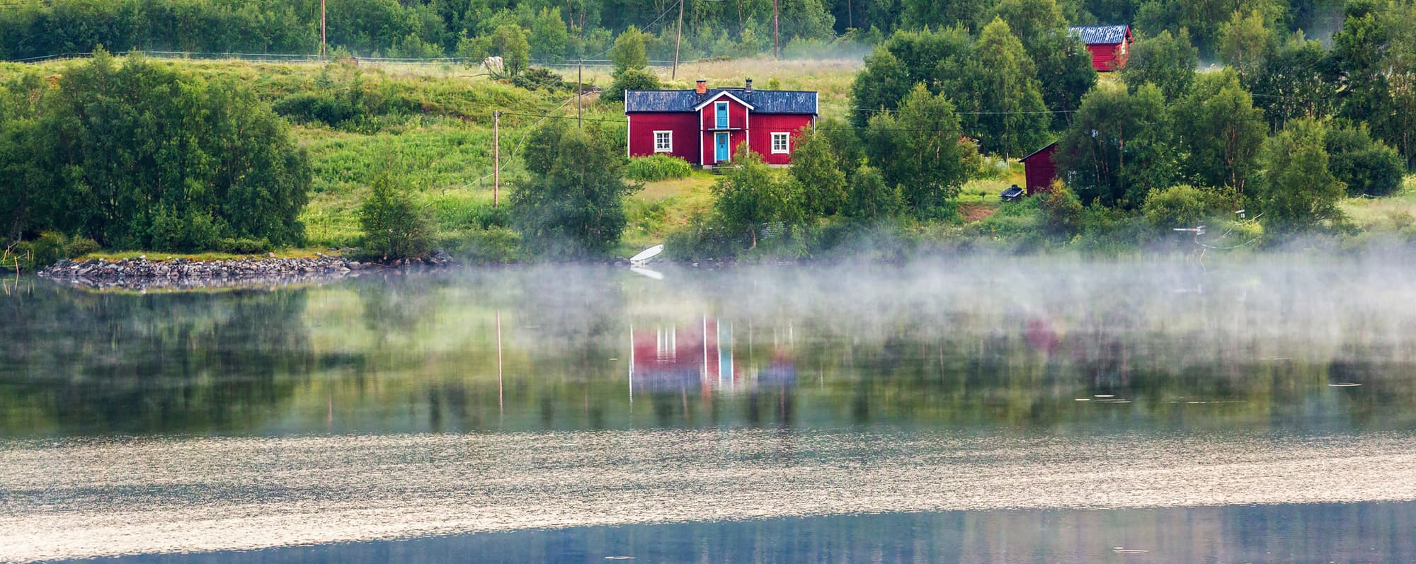 En röd stuga vid liten sjö i svensk skog.