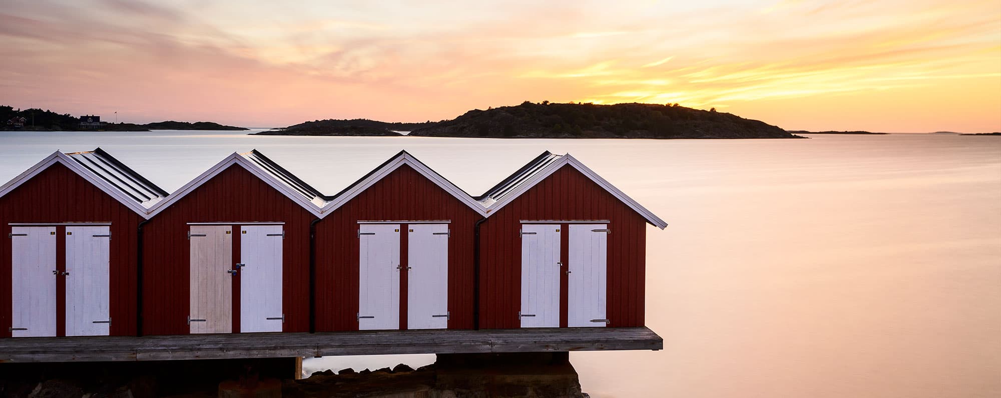 Svensk öl: Solnedgång i havet bakom små fiskebodar på en pir.