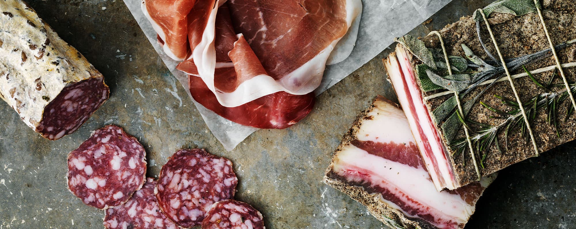 Grundsmaker symboliserade av salt pancetta, salami och lufttorkad skinka på stenhäll.