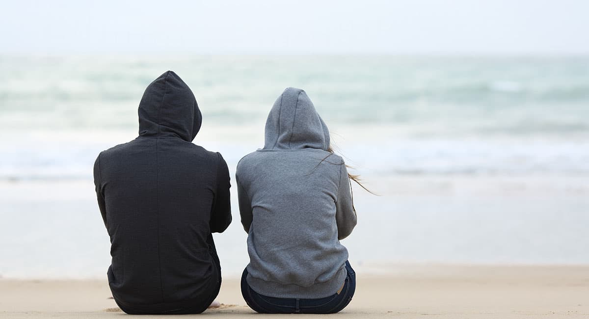 Två vänner sitter vid en strand och pratar.